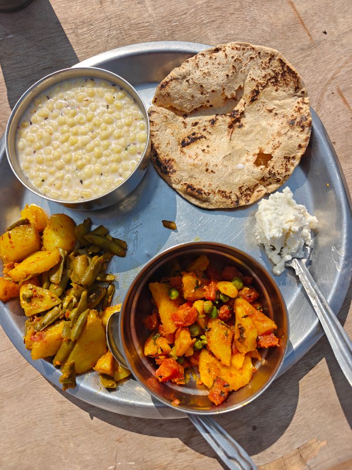 A home thali: roti, aloo and beans sabzi, aloo matar, and a katori of raita.